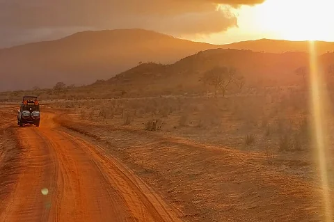 夕阳洒在一条橙色的土路上，一辆观光吉普车驶近，温暖的阳光照耀着干旱的景观。